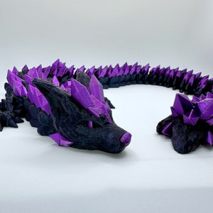 May include: A black and purple 3D printed dragon figurine with a spiky, crystal-like design. The dragon is curled into a circle shape with its head and tail facing each other.