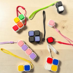 May include: A collection of colorful fidget toys in various shapes, including cubes and elongated designs. Each toy features multiple buttons in vibrant colors like red, yellow, and purple, attached to a lanyard. The toys are designed for tactile engagement.