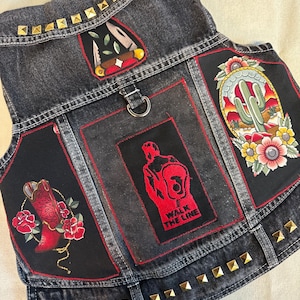 May include: Black denim vest with gold studs and various embroidered patches. The patches include a cactus, a cowboy boot, a knife, and a hand with the text "Walk the Line".
