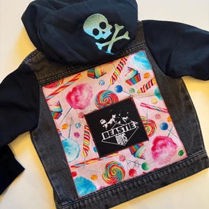 May include: Black denim jacket with a candy-themed fabric patch on the back. The patch features colorful lollipops, candy canes, and cotton candy. The patch also includes a black diamond-shaped patch with the text "BEASTIE BOYS" in white.
