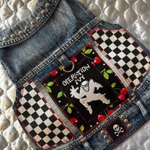 May include: A denim vest with silver studs along the collar. Patches include black and white checkered patterns, a black patch with the text "OPERATION IVY" and a graphic, and a skull and crossbones patch.