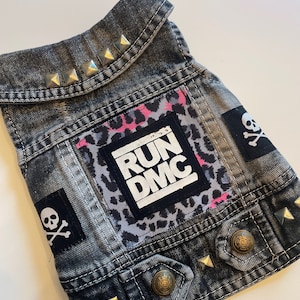 May include: A black denim vest with silver studs, a leopard print patch, and a white patch with the text "RUN DMC".