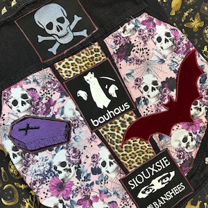 May include: A black denim jacket with various patches, including a skull and crossbones, a coffin, a bat, a leopard print, and a patch that says "bauhaus". There is also a patch with the text "Siouxsie and the Banshees".