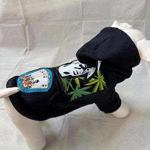 May include: Black hooded sweatshirt for a dog with a marijuana leaf design, a skull and crossbones design, and a playing card design with roses.