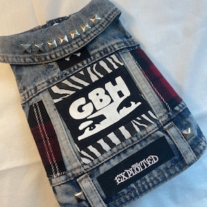 Puede incluir: Una chaqueta vaquera azul con parches, incluyendo un parche de estampado de cebra con el texto "GBH" y un parche negro con el texto "The Exploited". La chaqueta tiene tachuelas plateadas alrededor del cuello y en la parte inferior.