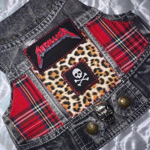 May include: A black denim vest with patches, studs, and skull accents. Features a Metallica logo patch, leopard print, and red plaid. Includes metal studs and skull-shaped button.