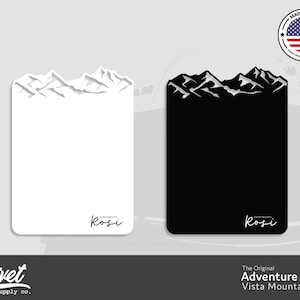 May include: Two versions of a white and black mountain range design on a rectangular board. The design is a silhouette of a mountain range with a white "Rosi" signature at the bottom. The text "The Original Adventure Board Vista Mountain" is below the image.