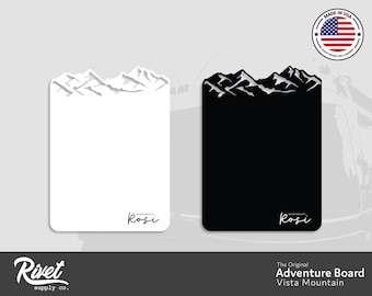 May include: Two versions of a white and black mountain range design on a rectangular board. The design is a silhouette of a mountain range with a white "Rosi" signature at the bottom. The text "The Original Adventure Board Vista Mountain" is below the image.