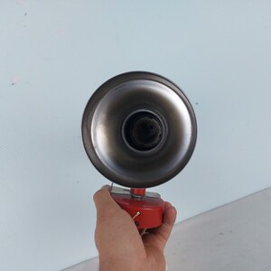 May include: A vintage metal lamp with a red base and a silver reflector. The lamp is held in a hand.