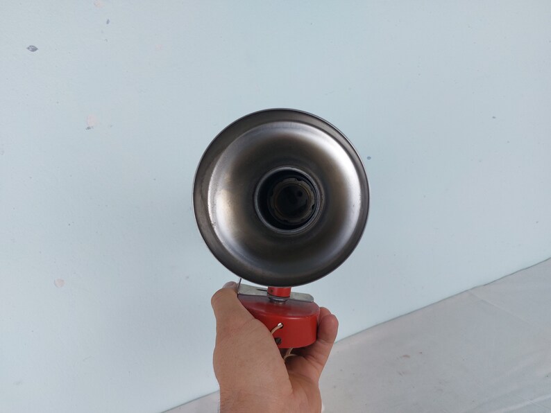 May include: A vintage metal lamp with a red base and a silver reflector. The lamp is held in a hand.