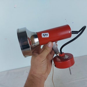 May include: A red and chrome wall-mounted lamp with a flexible arm and a round base. The lamp has a chrome reflector and a red cord. The lamp is labeled "189".