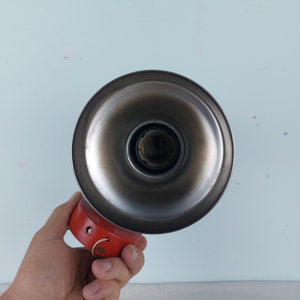 May include: A vintage metal lampshade with a red base and a silver reflector. The lampshade has a simple design and is perfect for adding a touch of retro style to any room.