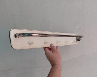May include: A white wooden wall-mounted coat rack with a chrome bar and five hooks. The rack is mounted on a white wall.