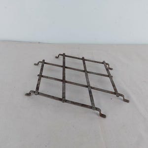Puede incluir: Una rejilla de metal con un patrón de diamante. La rejilla está hecha de finas varillas de metal soldadas entre sí. La rejilla está oxidada y tiene un aspecto desgastado.