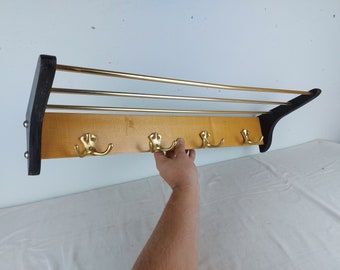 May include: A wooden coat rack with a black frame and four gold hooks. The rack has three horizontal brass bars.