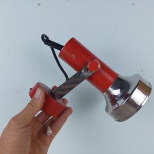 May include: A red and chrome adjustable wall lamp with a black cord. The lamp has a round base and a long, thin arm that can be moved up and down.