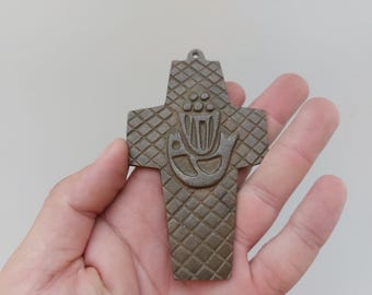 May include: A brown metal cross with a stylized design of a fish and a flower. The cross has a diamond pattern on the surface.
