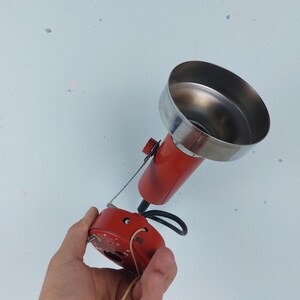 May include: A red and silver vintage lamp with a metal shade and a cord with a pull chain switch. The lamp is held in a hand.