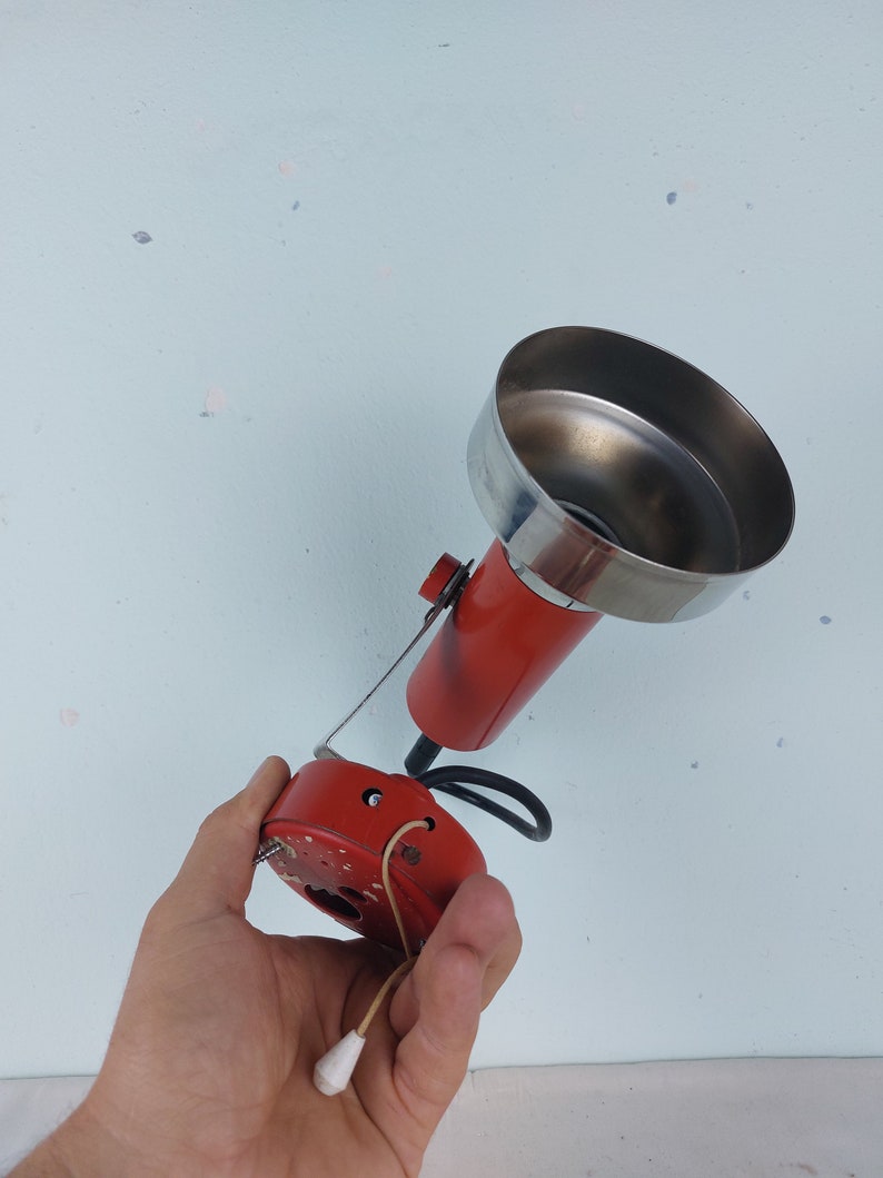 May include: A red and silver vintage lamp with a metal shade and a cord with a pull chain switch. The lamp is held in a hand.