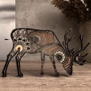 May include: A decorative wooden reindeer sculpture with intricate mandala-style patterns. The reindeer is made of layered wood in shades of brown and black, with a detailed design. The antlers are also made of wood. The sculpture is a unique home decor item.