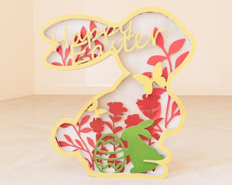 May include: A yellow papercraft bunny with the words "Happy Easter" cut out of the paper. The bunny is surrounded by red and green paper flowers and butterflies.