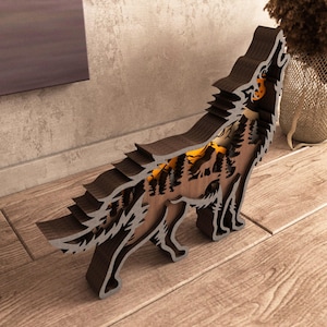 May include: A wooden wolf sculpture with a layered design, featuring a howling wolf silhouette. The sculpture has a dark brown exterior and a lighter brown interior with a forest scene. The sculpture is illuminated with a warm, orange glow.