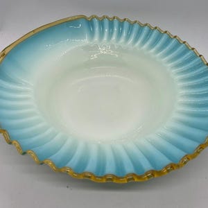 Op de afbeelding: Een ovale kom met een geschulpte rand, met een kleurovergang. De kom verloopt van lichtblauw naar wit in het midden, met een gouden rand. De kom heeft een geribbelde textuur. Waarschijnlijk van glas.