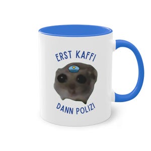 Op de afbeelding: Witte keramische mok met een blauwe rand en handvat. De mok heeft een cartoonafbeelding van een maki met een politiepet en de tekst "ERST KAFFI DANN POLIZI".