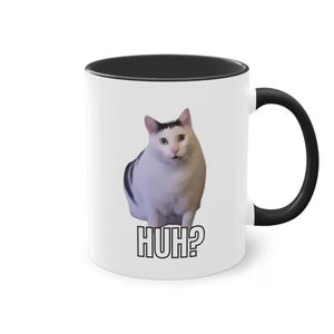 May include: White ceramic coffee mug with a black rim and handle. The mug features a photo of a white cat with black markings, looking surprised, with the text "HUH?" printed below the image.