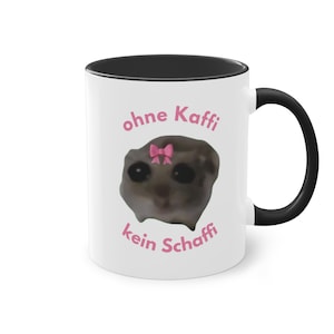 Könnte beinhalten: Weiße Keramik-Kaffeetasse mit schwarzem Rand und Henkel. Die Tasse zeigt ein Cartoon-Bild eines traurigen Tieres mit einer rosa Schleife auf dem Kopf. Der Text "ohne Kaffe kein Schaffi" ist auf die Tasse gedruckt.