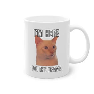 Könnte beinhalten: Weiße Keramik-Kaffeetasse mit einem Katzenbild und dem Text "Ich bin hier für das Drama".
