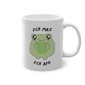Könnte beinhalten: Weiße Keramiktasse mit einem grünen Frosch-Cartoon, der den Mittelfinger zeigt. Der Text auf der Tasse lautet "FCK MRZ" und "FCK AFD".