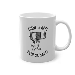 Könnte beinhalten: Weiße Keramik-Tasse mit einer schwarzen Grafik eines Hundes, der einen Kaffeefilter hält, mit dem Text "OHNE KAFFI KEIN SCHAFFI". Die Tasse hat einen gebogenen Henkel.