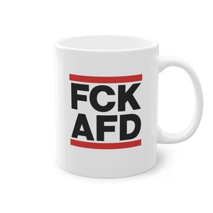 Könnte beinhalten: Weiße Keramik-Kaffeetasse mit schwarzem Text, der "FCK AFD" lautet, mit zwei roten Linien über und unter dem Text.