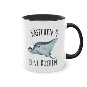 Könnte beinhalten: Eine weiße Keramiktasse mit schwarzem Innenraum und Henkel. Die Außenseite zeigt eine Illustration eines blauen Rochens, der eine Kaffeetasse und eine Zigarette hält, mit dem Text KÄFFCHEN & EENE ROCHEN in schwarzer Schrift darüber und darunter.