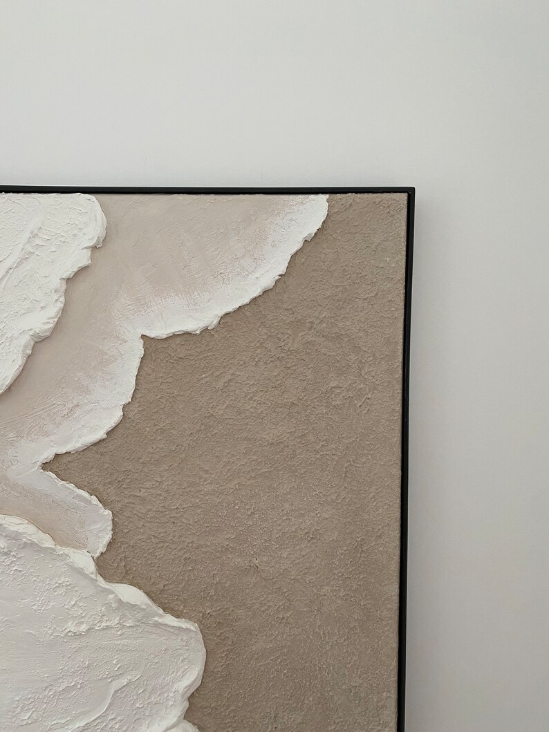 May include: Abstract painting with textured white and beige paint on a canvas with a black frame.