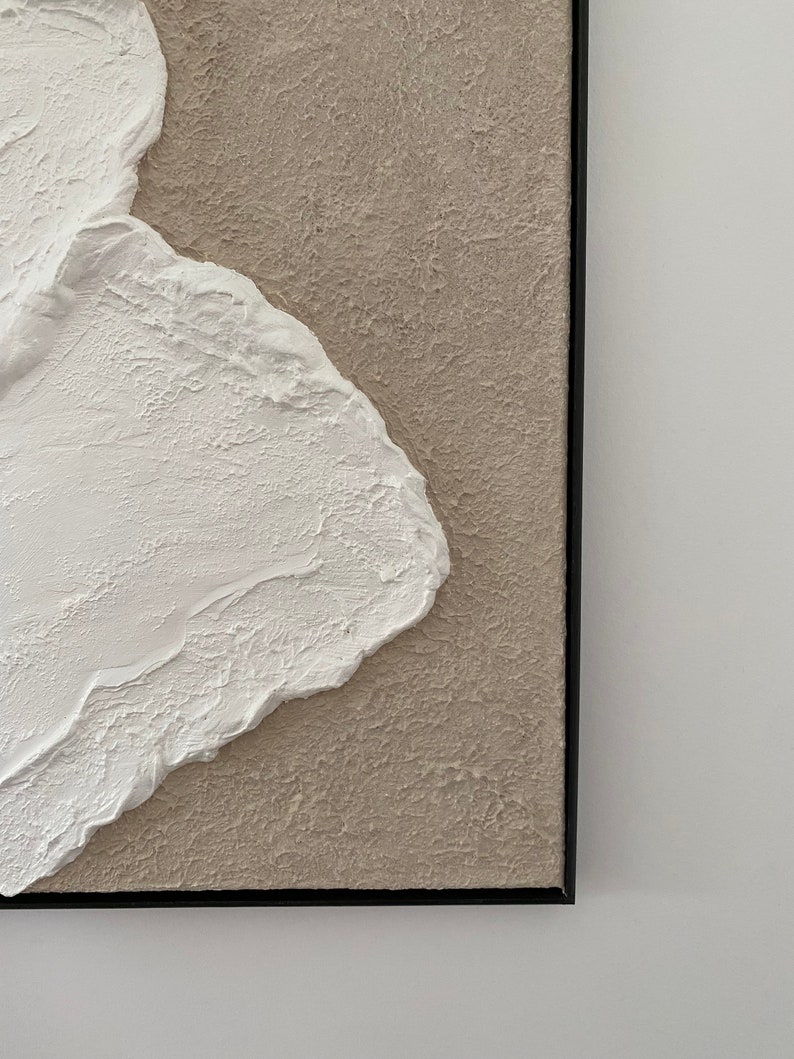 May include: Abstract painting with a textured white shape on a beige background. The painting is framed in black.