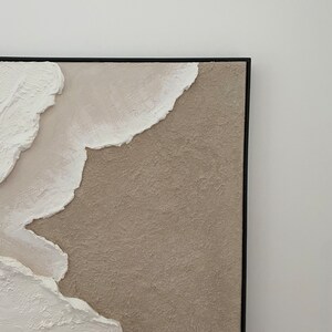 May include: Abstract painting with textured white and beige paint on a canvas with a black frame.