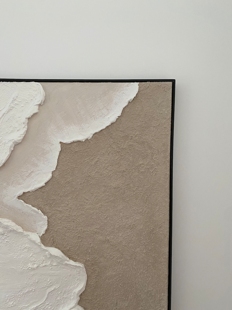 May include: Abstract painting with textured white and beige paint on a canvas with a black frame.