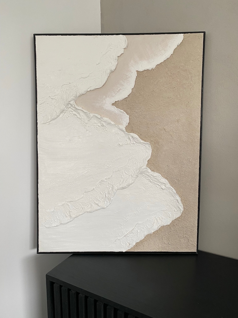 May include: Abstract painting with textured white and beige paint in a black frame.
