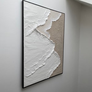May include: Abstract painting with white and beige textured paint on canvas, framed in black.