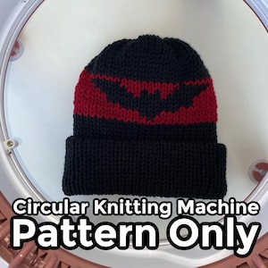 Op de afbeelding: Een zwarte gebreide beanie met een rood vleermuisvormig ontwerp. De hoed wordt getoond op een rondbreimachine. De tekst op de afbeelding luidt "Circular Knitting Machine Pattern Only."