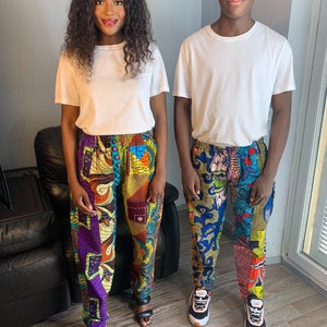 Puede incluir: Dos personas con camisetas blancas y pantalones con estampados coloridos. La mujer lleva sandalias negras. El hombre lleva zapatillas blancas y naranjas.