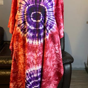 Könnte beinhalten: Ein rot-violetter Batik-Kaftan mit einem kreisförmigen Muster. Der Kaftan befindet sich auf einem Mannequin und hat eine lockere, fließende Passform.