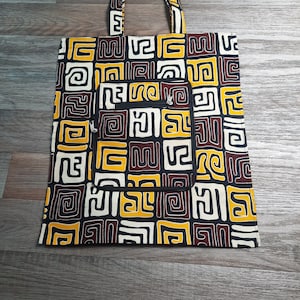 Peut inclure: Un sac fourre-tout noir et blanc avec un motif géométrique brun et jaune. Le sac a une petite poche zippée sur le devant.