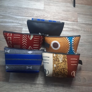 Puede incluir: Seis bolsas de cosméticos con diferentes patrones y cremalleras negras. Las bolsas están hechas de tela con varios diseños geométricos y abstractos en tonos de rojo, naranja, azul, amarillo y marrón.