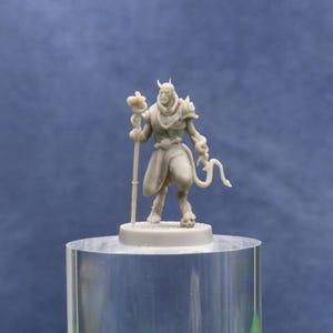May include: A gray miniature figurine of a horned humanoid figure with a staff and a tail. The figure is standing on a clear acrylic cylinder against a blue background. The figurine has a detailed design.