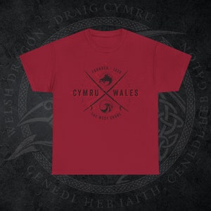 May include: A red t-shirt with a black graphic design featuring the words "CYMRU WALES" and "THE WEST SHORE". The design includes crossed lines, a dragon, and the text "FOUNDED 1536".