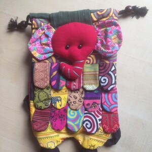 Può includere: Una borsa a cordoncino a forma di elefante in patchwork colorato con una testa di elefante in feltro rosso e piedi in feltro nero. La borsa è realizzata con diversi tessuti con motivi e colori diversi, tra cui rosa, viola, giallo, verde e blu.