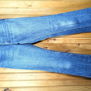 May include: A pair of blue denim jeans featuring a classic five-pocket design, a button fly closure, and a straight-leg cut. The denim has a medium-wash finish with subtle fading on the thighs and knees, and visible stitching along the seams.